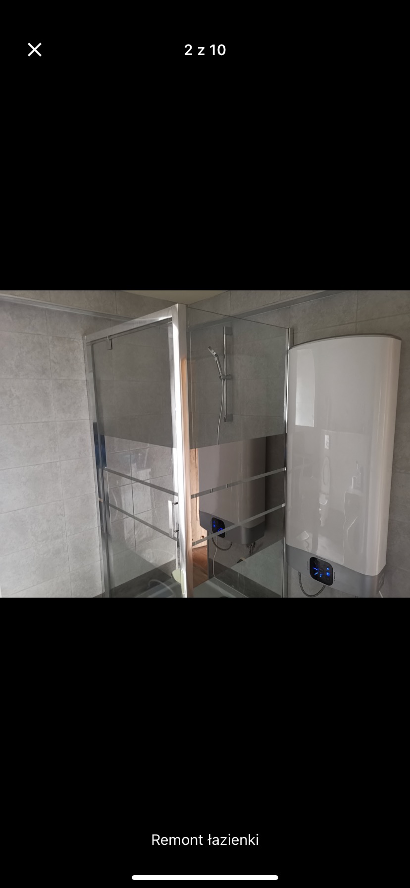 Wykończona łazienka z kabiną prysznicową ze srebrnymi ramami i dwoma białymi podgrzewaczami wody z niebieskimi wyświetlaczami na tle szarych płytek.