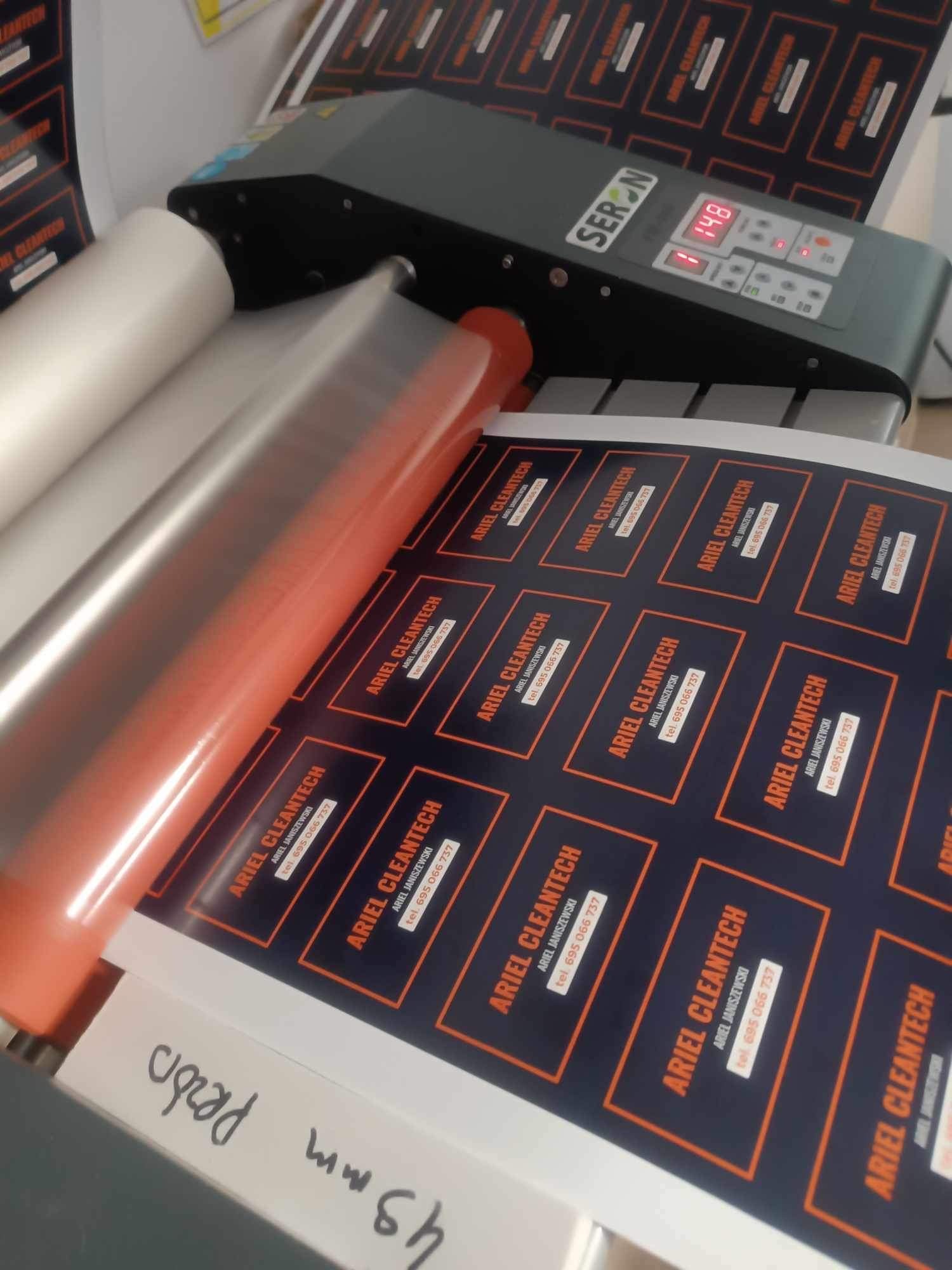 Laminowanie arkusza z naklejkami wizytówkami firmy Ariel Cleantech na maszynie SERON, widoczne rolki folii i panel sterowania z wyświetlaczem 148.