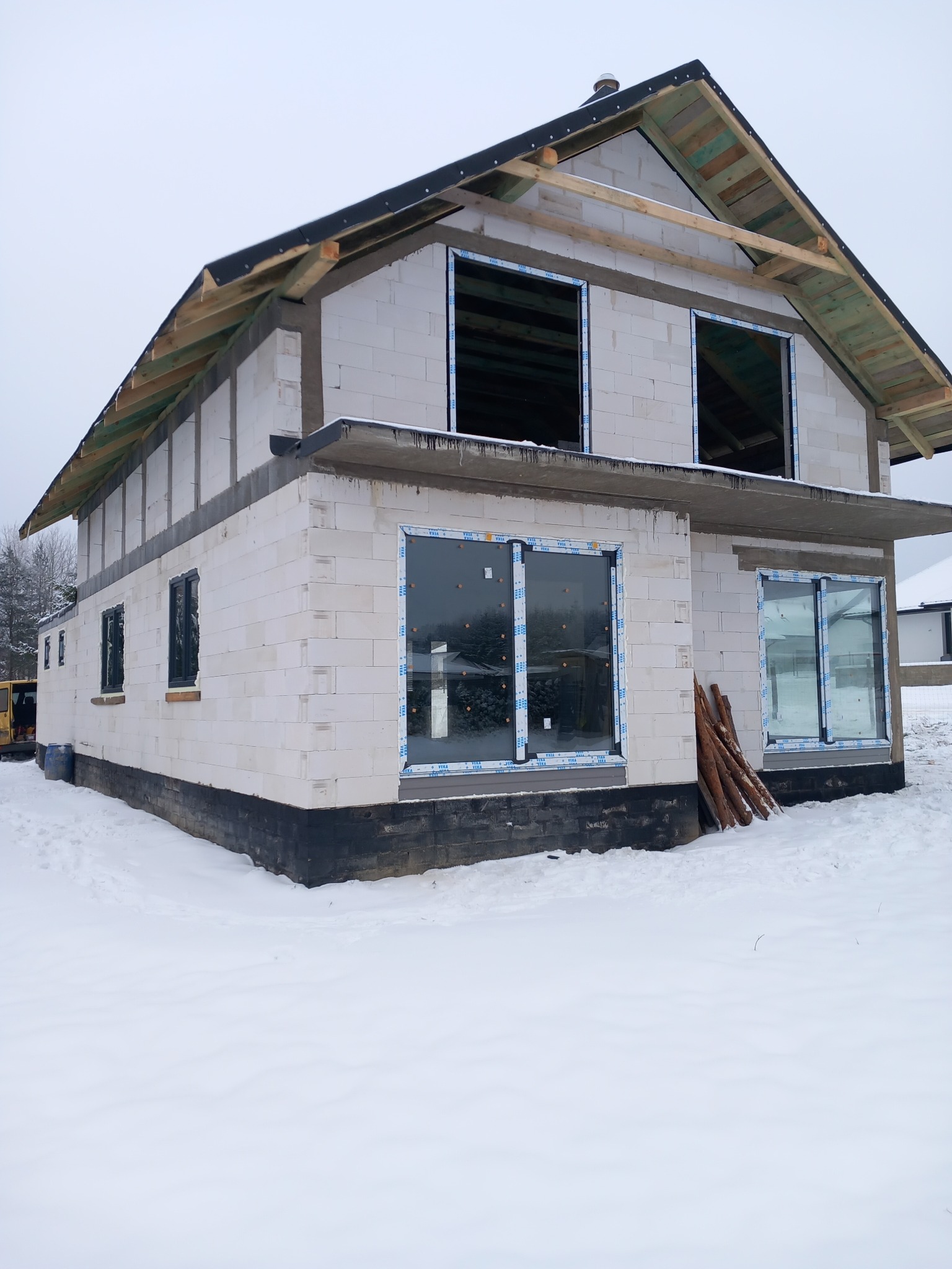 Surowy stan domu w zimowej scenerii z częściowo zamontowanymi oknami PCV i przygotowaną konstrukcją dachu.