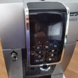 Automatyczny ekspres do kawy DeLonghi Amica z panelem sterowania, srebrno-czarny korpus, tacka ociekowa z metalowymi kratkami.