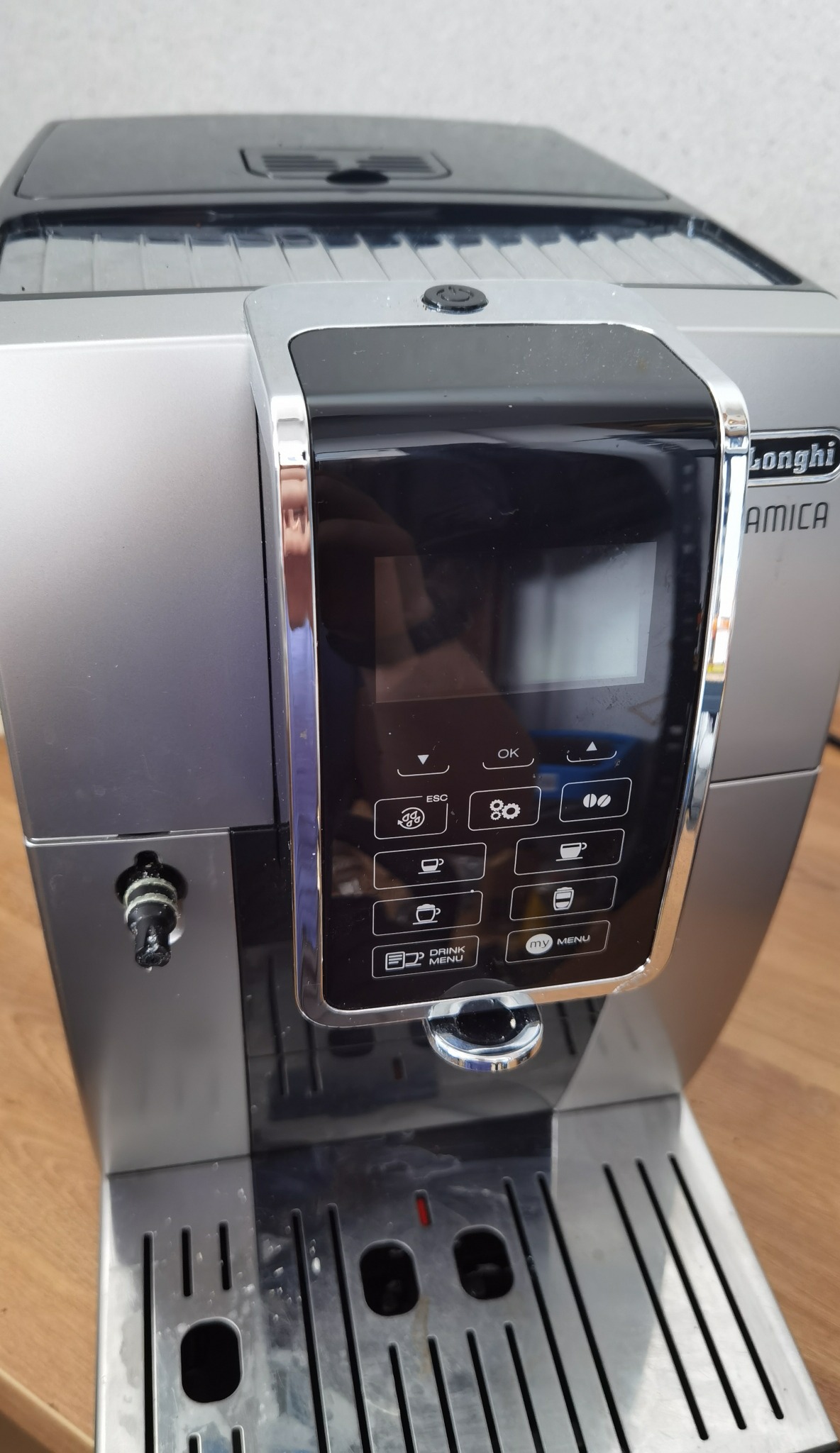 Automatyczny ekspres do kawy DeLonghi Amica z panelem sterowania, srebrno-czarny korpus, tacka ociekowa z metalowymi kratkami.