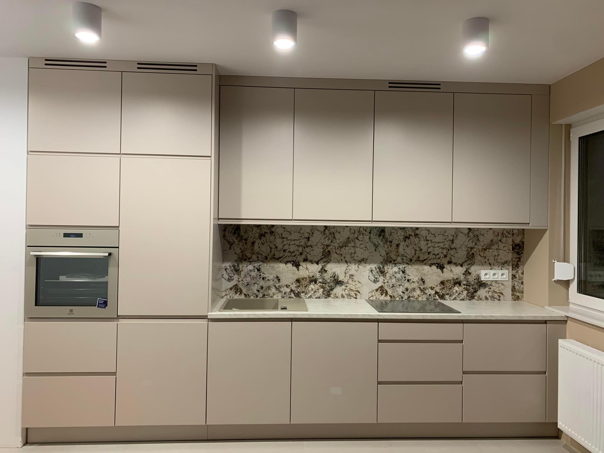 Nowoczesna zabudowa kuchenna w odcieniach beżu z marmurkowym panelem nad blatem, oświetleniem punktowym i wbudowanym piekarnikiem Electrolux