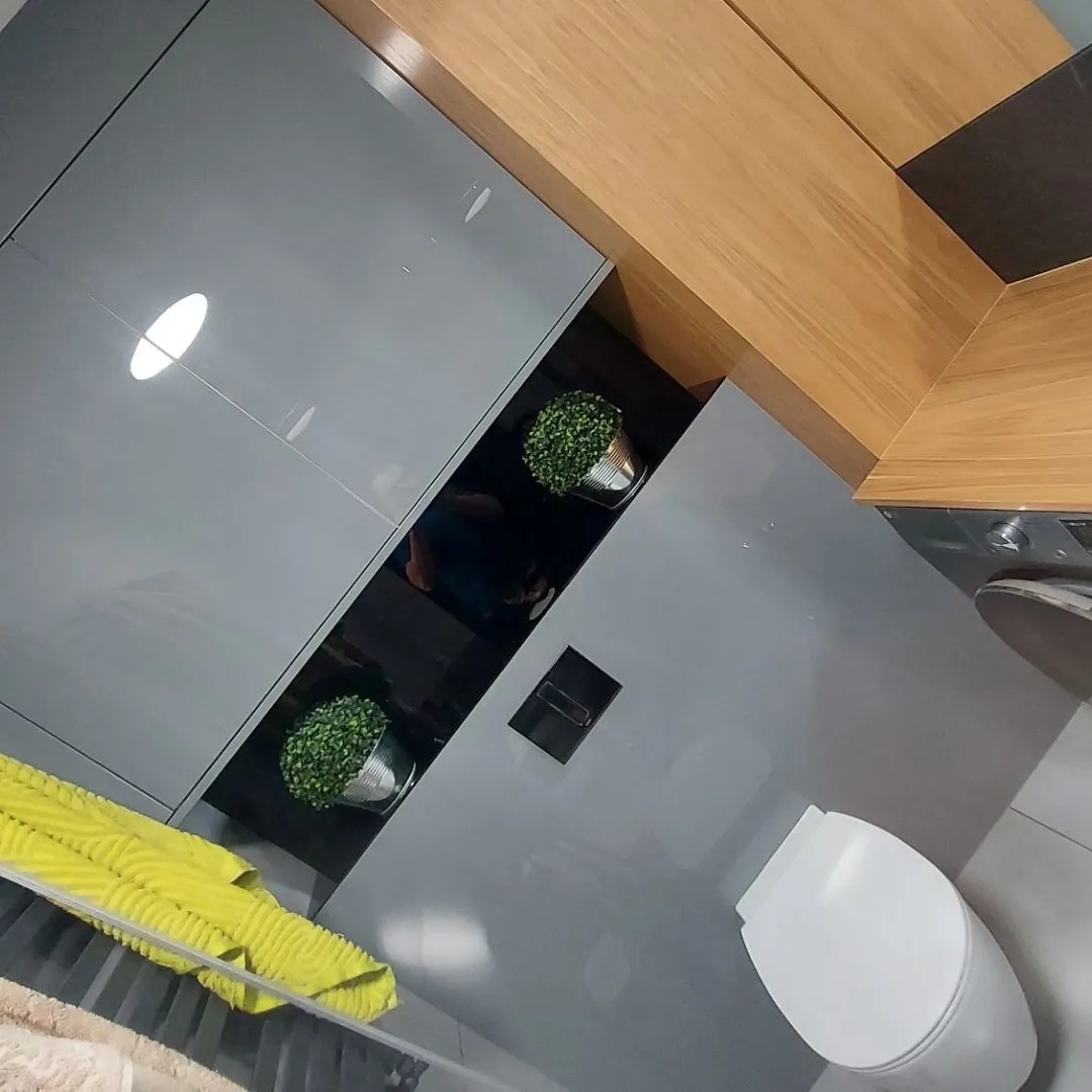 Nowoczesna łazienka z szarymi, lakierowanymi szafkami, drewnianym blatem i dekoracyjnymi roślinami w metalowych doniczkach.