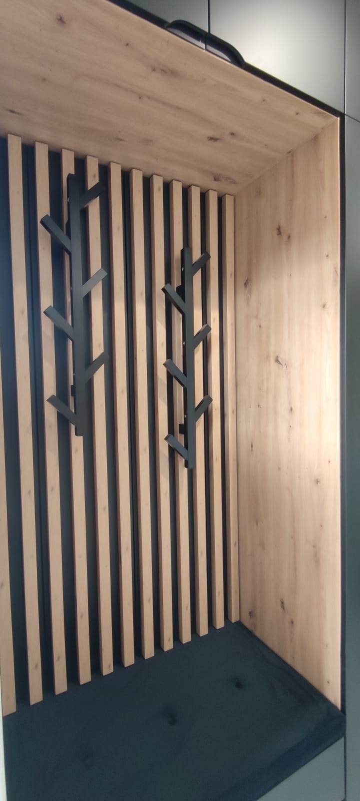 Wnęka z siedziskiem wykończona drewnem i lamelami z wieszakami w kształcie drzewek.