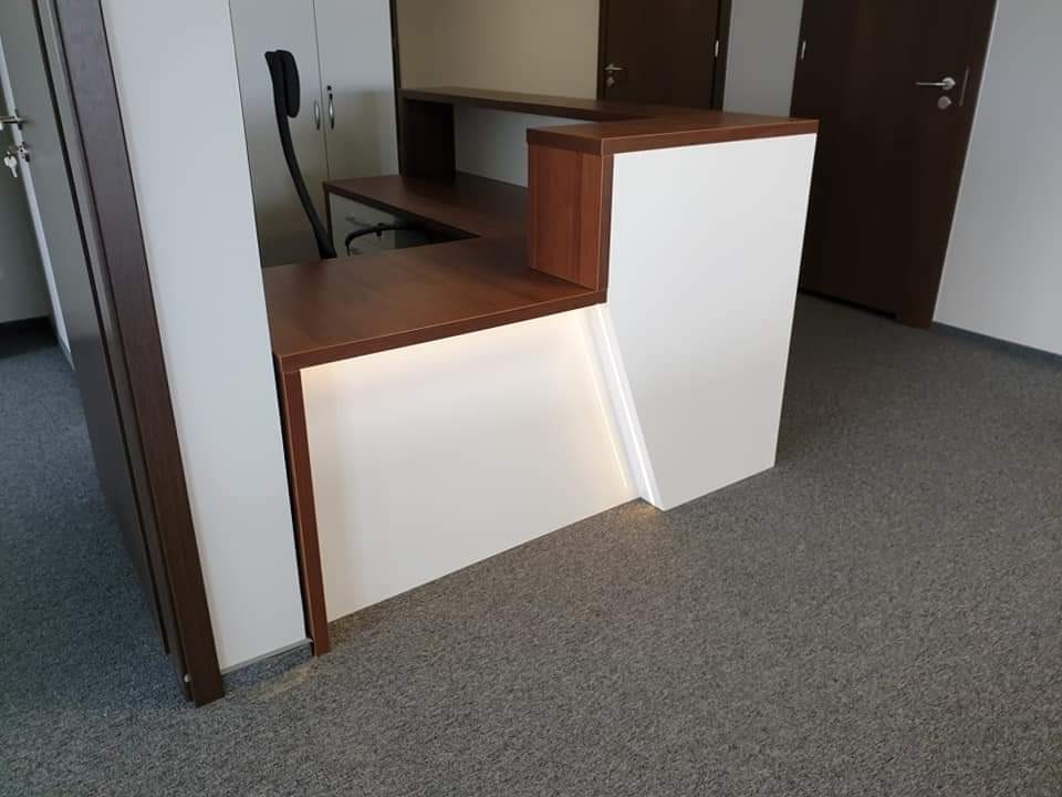 Biało-brązowa lada recepcyjna z podświetleniem LED w dolnej części, widok z boku, na podłodze szary dywan biurowy.