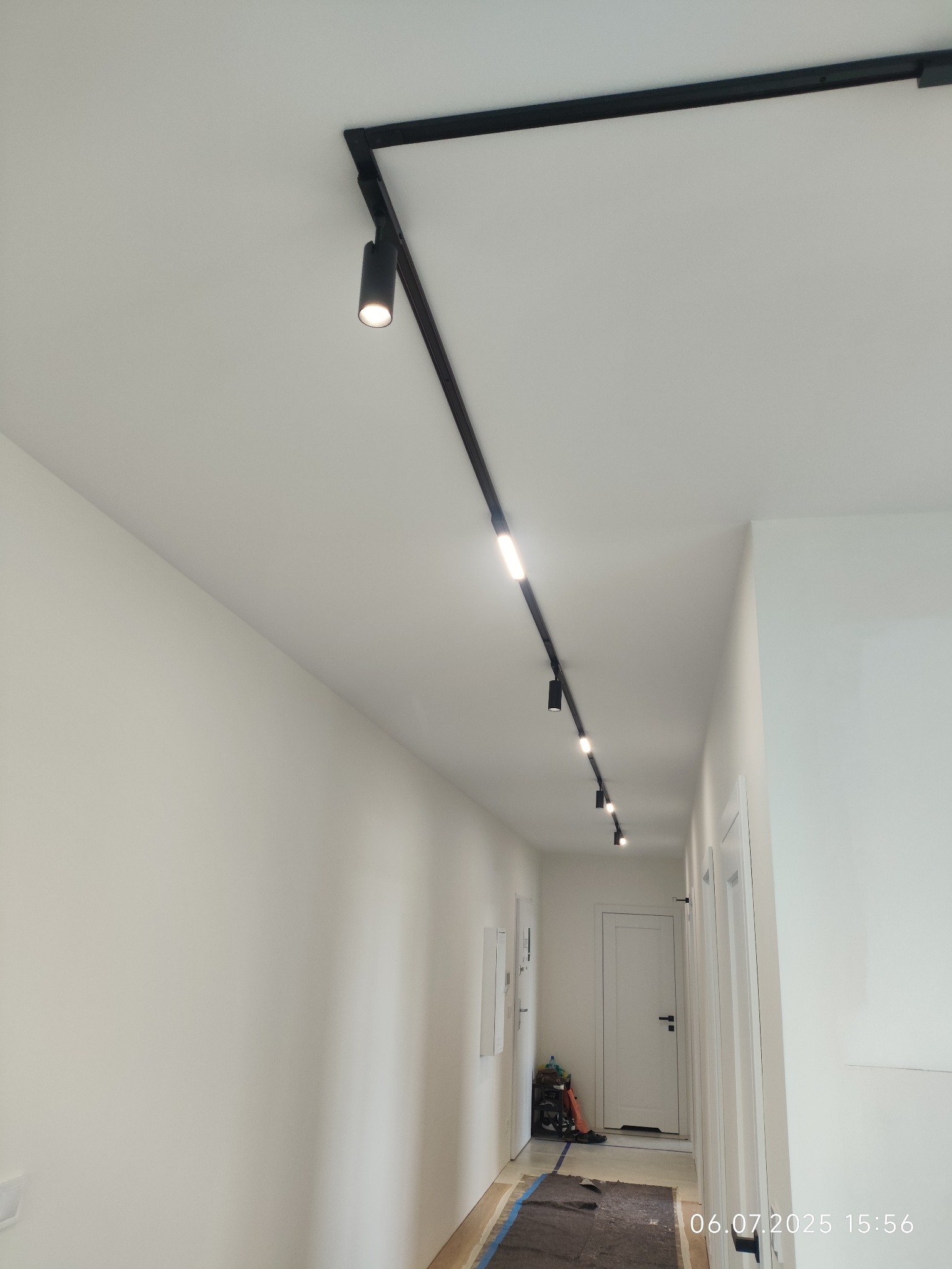 Nowoczesne oświetlenie szynowe, czarne reflektory punktowe na białym suficie, korytarz w minimalistycznym stylu, widok z dołu, równomierne rozmieszczenie lamp.