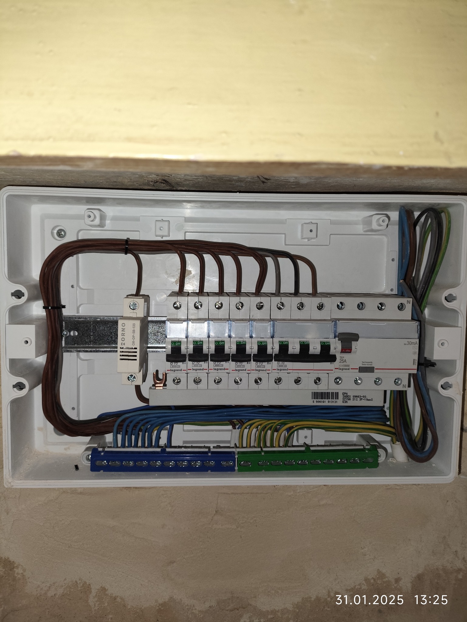 Rozdzielnia elektryczna w białej obudowie, z widocznymi bezpiecznikami i przewodami. Instalacja wewnątrz budynku, przed wykończeniem ścian.