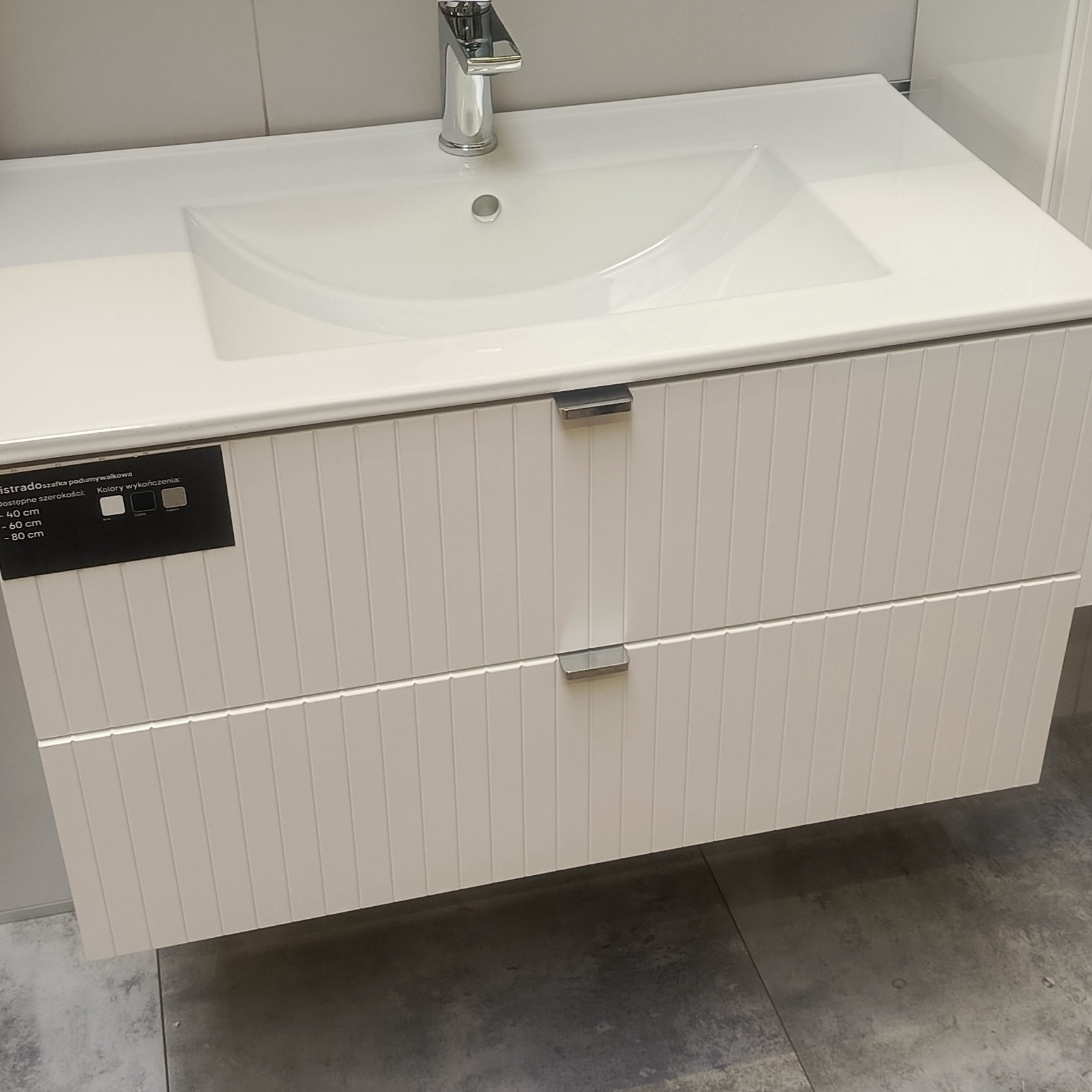 Biała szafka pod umywalkę z chromowanym kranem. Nowoczesny design wykończenia łazienki w Mysłowicach. Widoczne detale wykończenia i subtelne uchwyty.