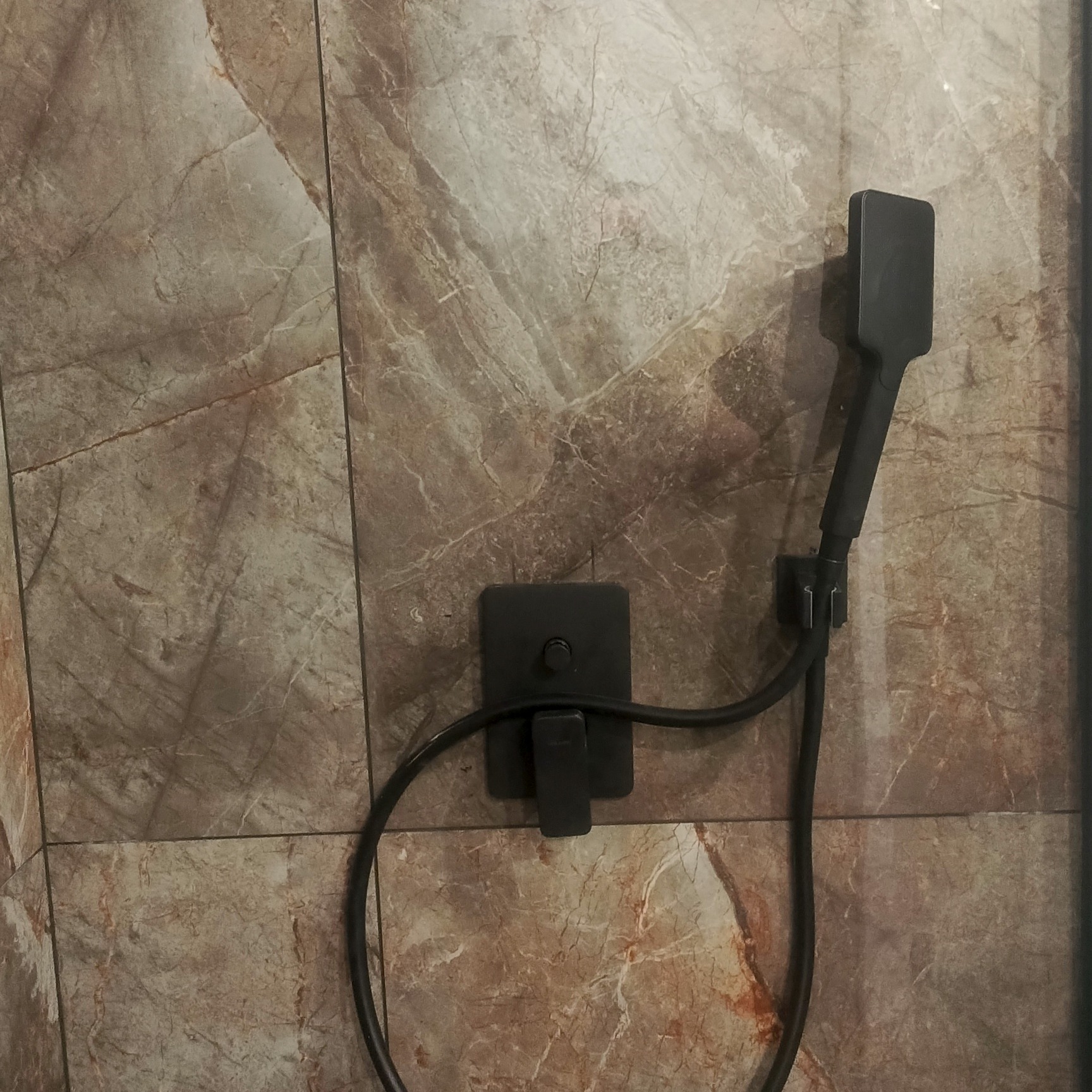 Nowoczesna, matowa, czarna bateria prysznicowa z deszczownicą na ścianie z płytek imitujących marmur w odcieniach beżu i brązu. Minimalistyczny design.