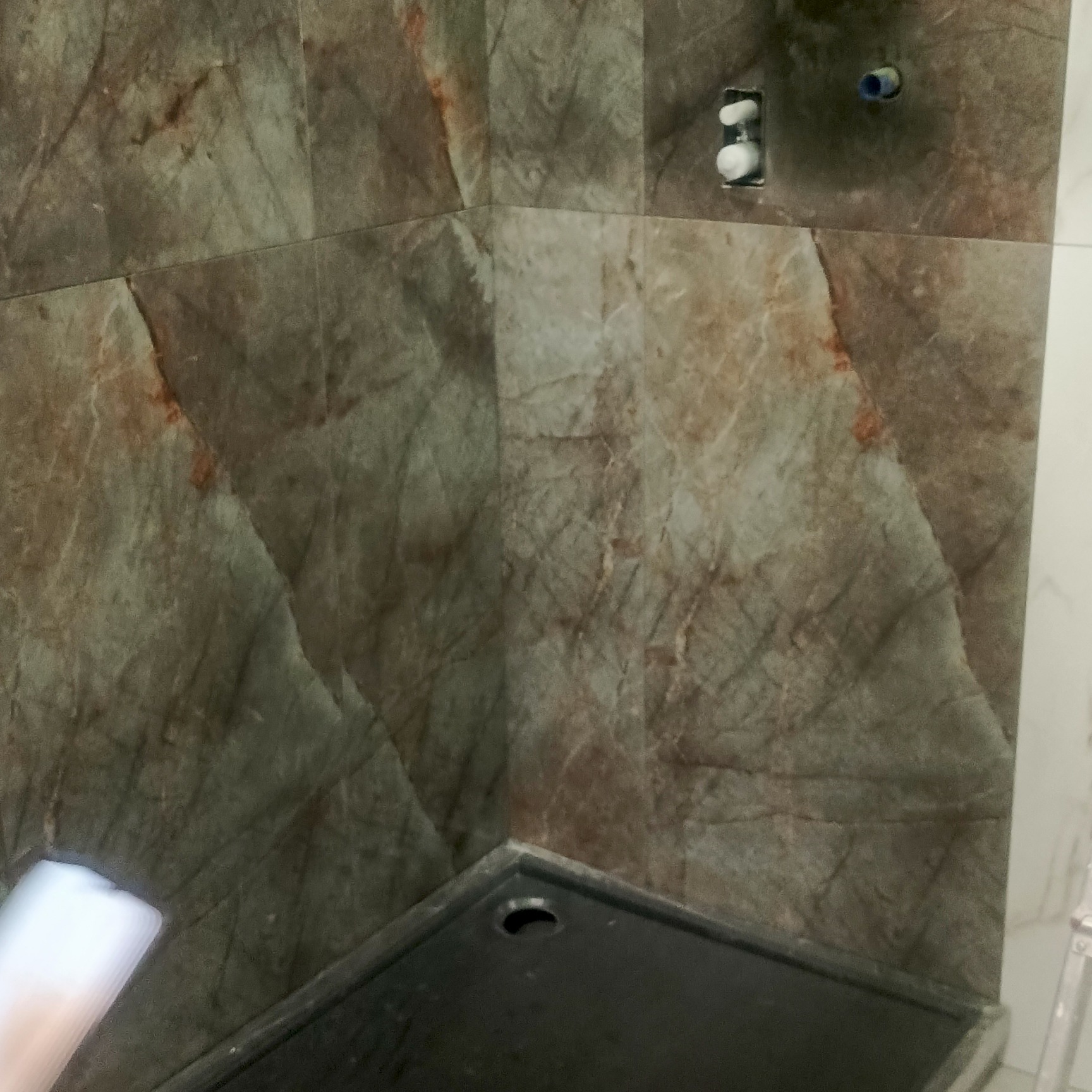 Wykończona ściana w łazience z brązowych, marmurkowych płytek, widoczne przyłącza wodne i fragment brodzika.