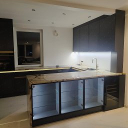 Lukasz Fabisiak - Nowoczesna kuchnia z wyspą, fronty szafek w kolorze grafitowym z delikatnym wzorem, marmurowy blat, szklane witryny z podświetleniem LED. Eleganckie wykończenie.