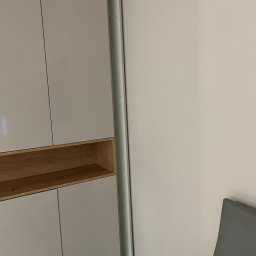 Lukasz Fabisiak - Jasna szafa wnękowa z drewnianą półką, dopasowana do ściany, widoczna z bliska. Minimalistyczny design, gładkie fronty, subtelne oświetlenie.