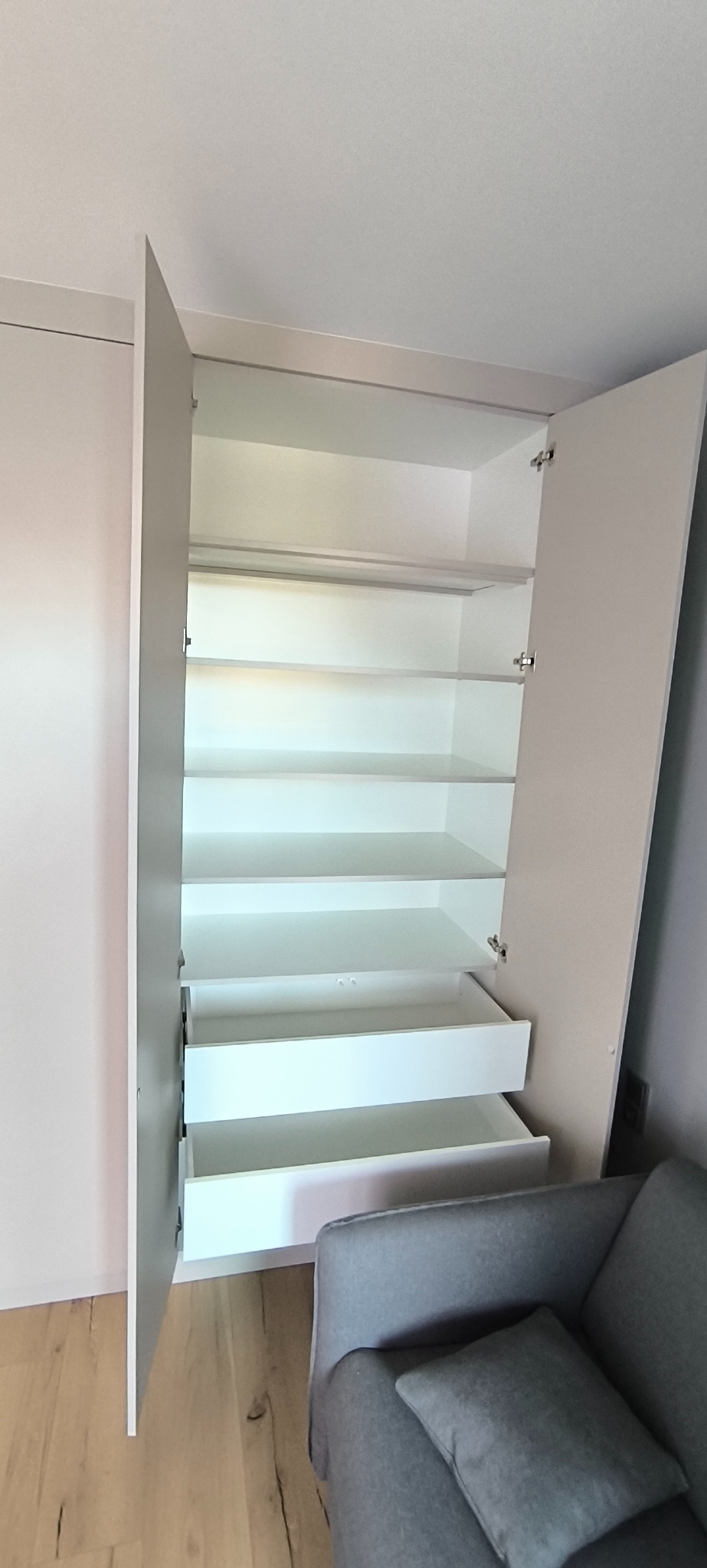 Jasna szafa wnękowa z otwartymi drzwiami i szufladami, widoczna z perspektywy wnętrza, Szczecin. Minimalistyczny design, neutralna kolorystyka, nowoczesne wykończenie.