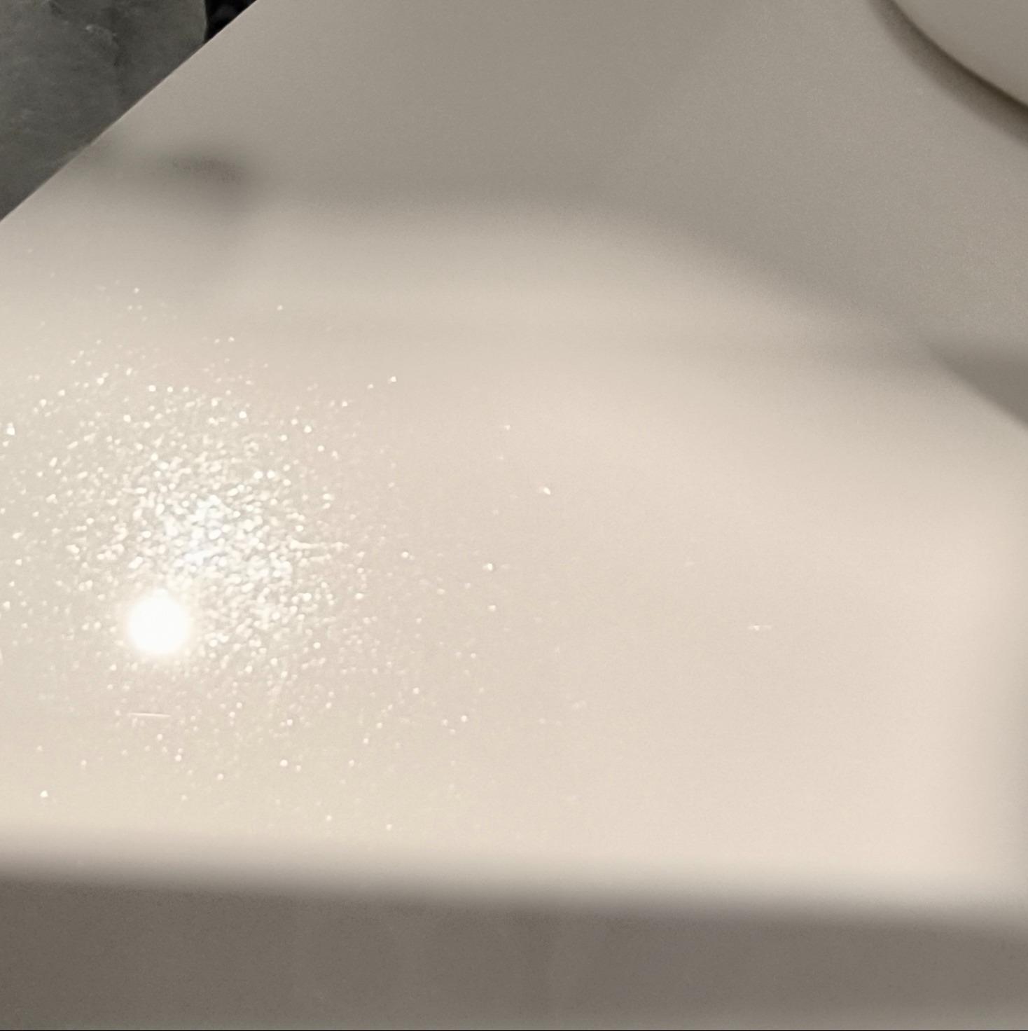 Biały, błyszczący blat meblowy z delikatnymi refleksami światła, ukazujący gładką powierzchnię i minimalistyczny design. Fragment blatu z widoczną strukturą.