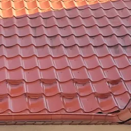 Czerwona blachodachówka na dachu domu w Lipinach, widoczna również rynna w tym samym kolorze, częściowo zabrudzona powierzchnia dachu.