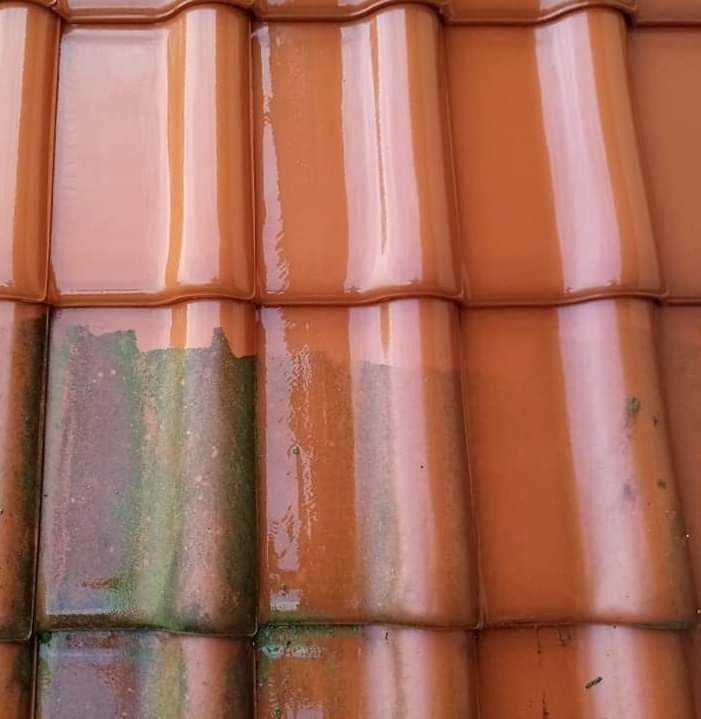 Częściowo umyte, mokre, pomarańczowe dachówki ceramiczne z widocznym zielonym nalotem na niektórych elementach.