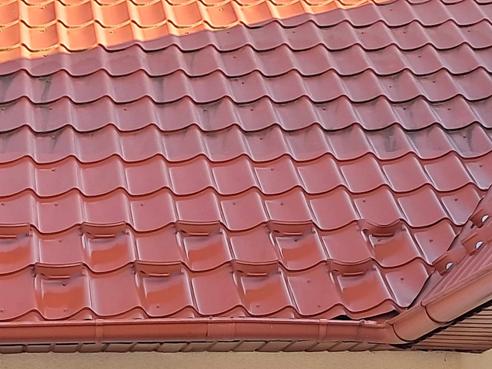 Czerwona blachodachówka na dachu domu w Lipinach, widoczna również rynna w tym samym kolorze, częściowo zabrudzona powierzchnia dachu.