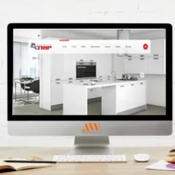 Monitor iMac wyświetlający stronę internetową z jasnym wnętrzem kuchni. Na biurku przed monitorem kaktus, notatnik i próbki kolorów.