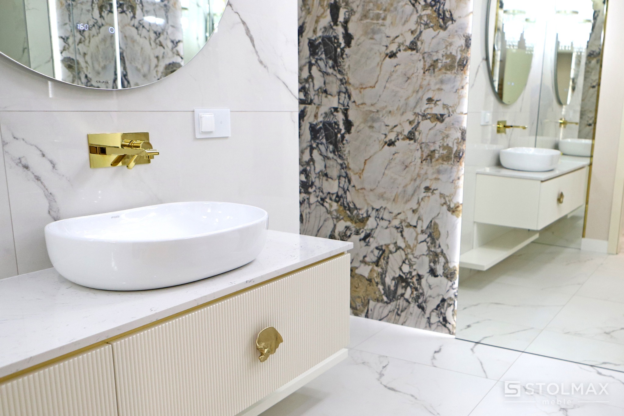 Nowoczesna łazienka z umywalką nablatową, złotą armaturą i marmurowym wykończeniem ścian oraz podłogi, widoczna szafka pod umywalkę z ryflowanym frontem i złotymi uchwytami.