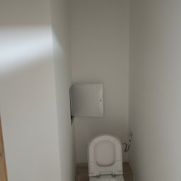 Akacjowa - Wąska toaleta po remoncie, z otwartą klapą sedesu i dostępem do zaworów, świeżo pomalowane ściany na biało.