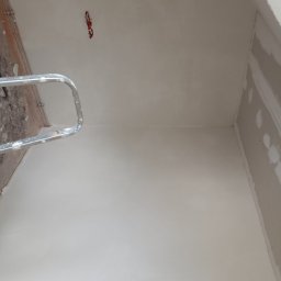 Akacjowa - Świeżo wygładzona ściana w trakcie remontu, widoczna drabina malarska, puszka elektryczna na suficie oraz fragment płyty gipsowo-kartonowej na ścianie bocznej.