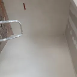 Świeżo wygładzona ściana w trakcie remontu, widoczna drabina malarska, puszka elektryczna na suficie oraz fragment płyty gipsowo-kartonowej na ścianie bocznej.