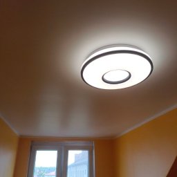 Akacjowa - Nowoczesna okrągła lampa sufitowa z czarnym obramowaniem, oświetlająca pomalowany na żółto pokój z oknem.