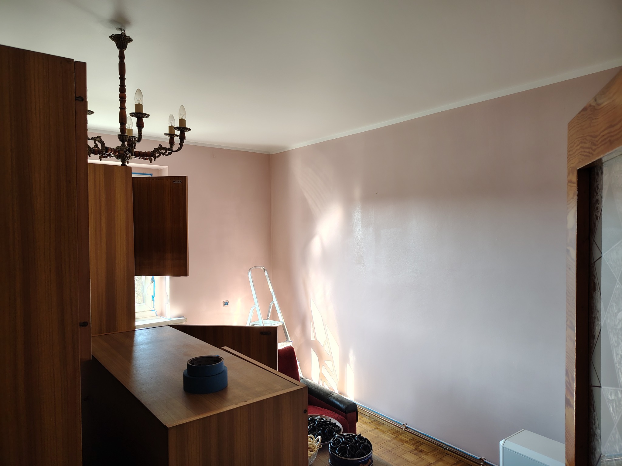 Pokój po malowaniu ścian na delikatny róż, widoczne ślady po taśmie malarskiej, drabina i meble w stylu vintage.