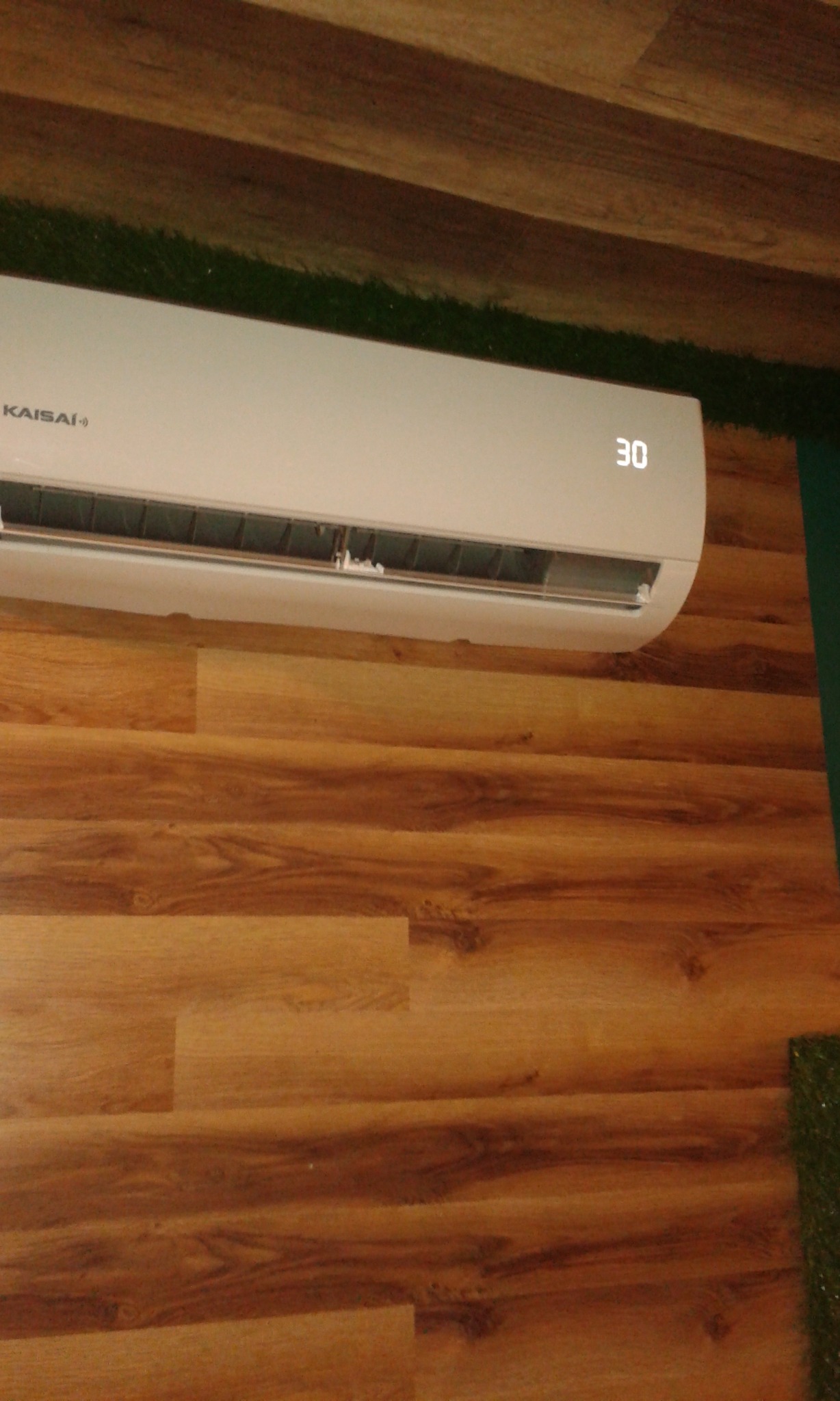 Biały klimatyzator marki Kaisai ustawiony na temperaturę 30 stopni Celsjusza, zamontowany na ścianie wykończonej panelami drewnopodobnymi w Lesznie.