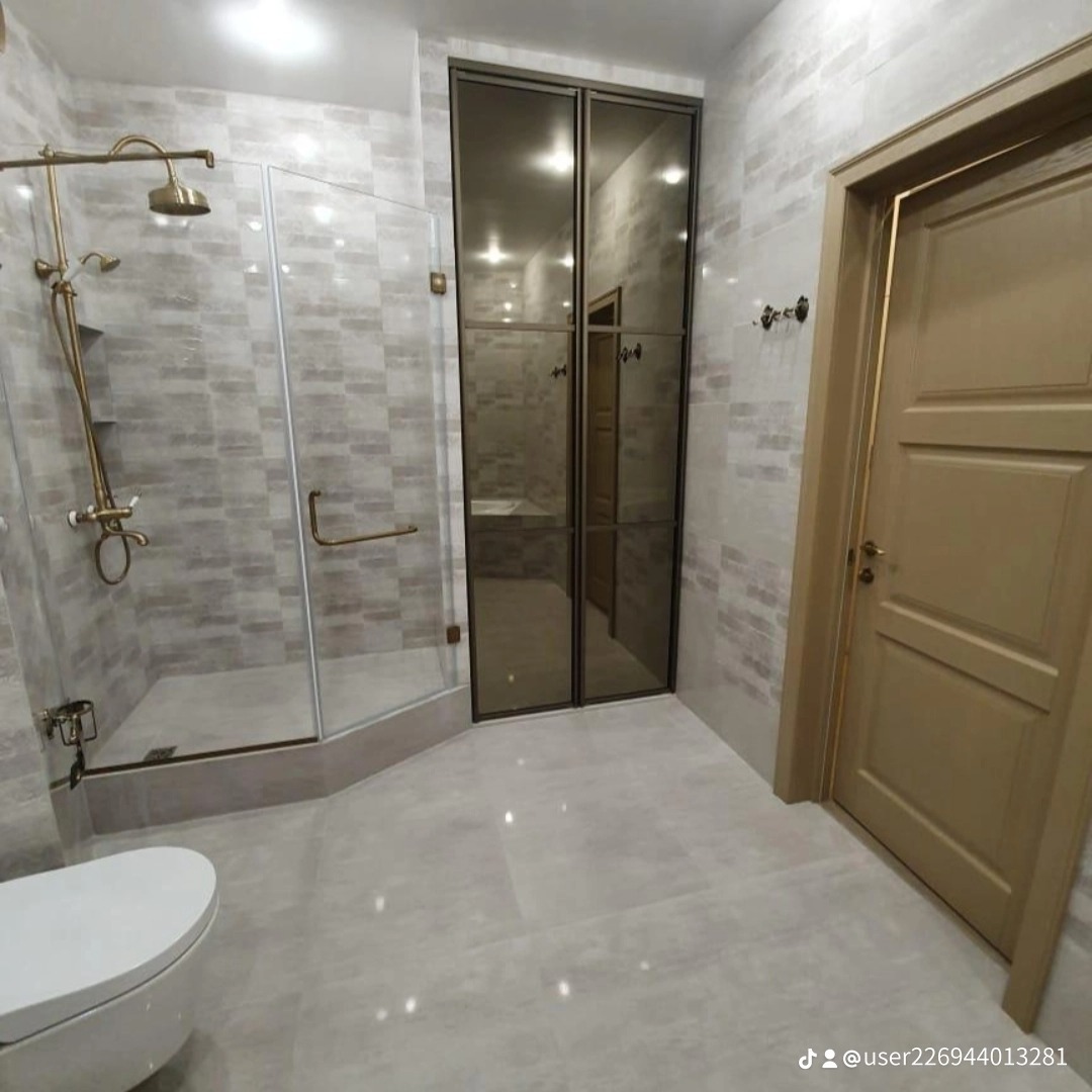 Nowoczesna łazienka z kabiną prysznicową typu walk-in z mosiężną armaturą, szklanymi drzwiami prysznicowymi i lustrzanymi drzwiami obok drewnianych drzwi wejściowych