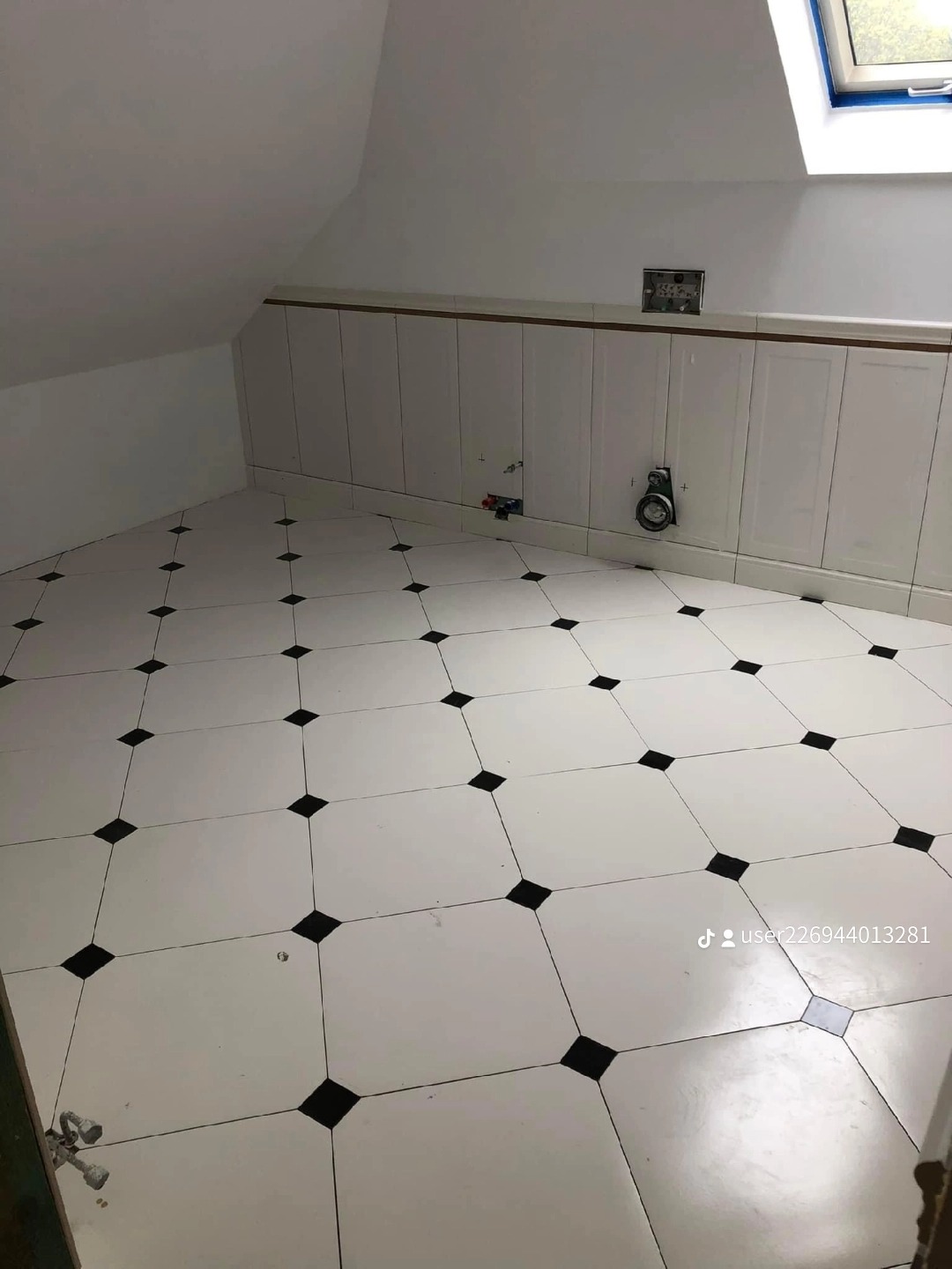 Poddasze po remoncie z biało-czarną podłogą w szachownicę i białymi panelami ściennymi, widoczne instalacje elektryczne i hydrauliczne przed montażem armatury.