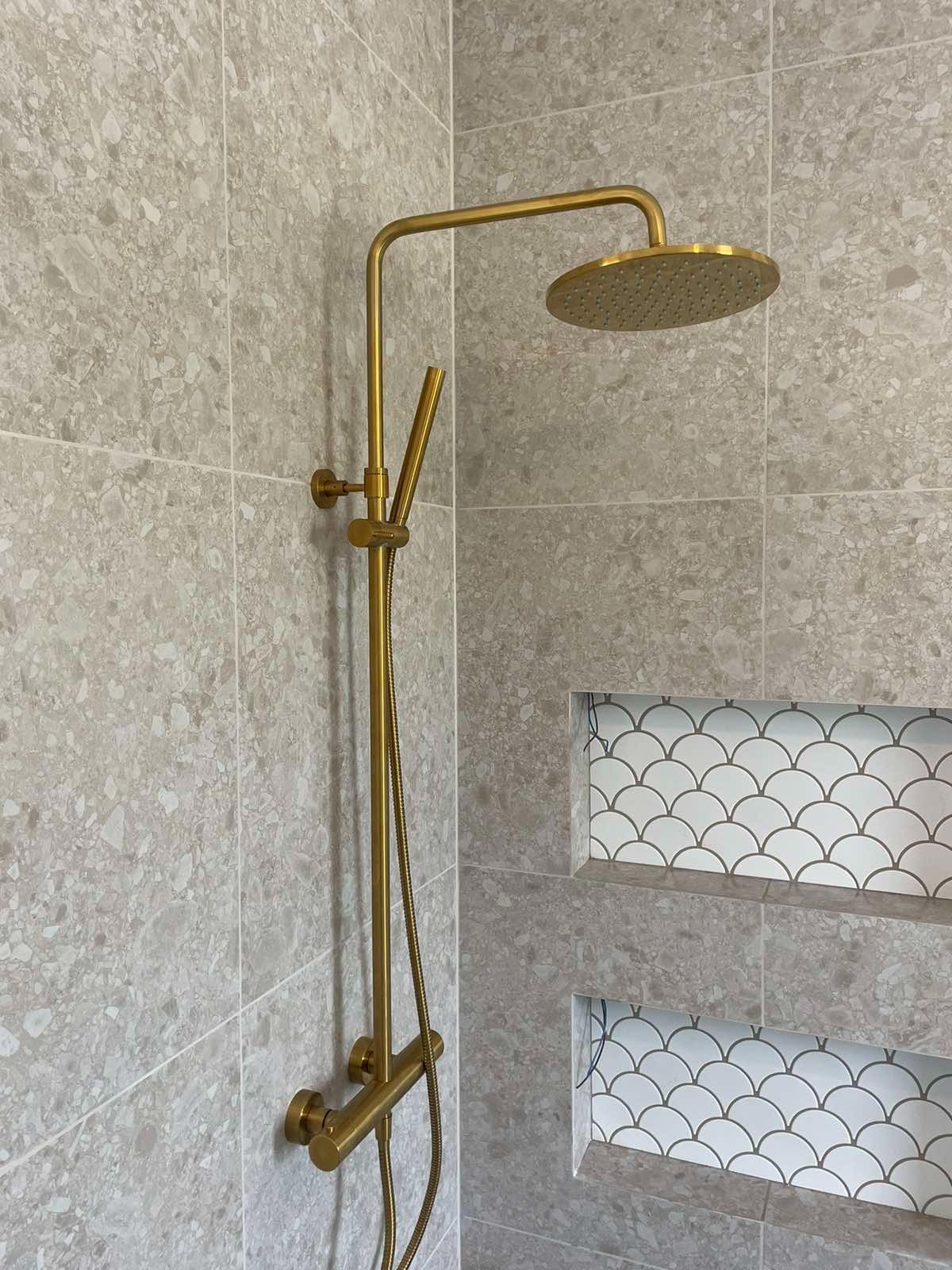 Nowoczesna łazienka w Warszawie z złotą armaturą prysznicową i półkami wyłożonymi mozaiką w kształcie rybiej łuski na tle szarych płytek imitujących kamień.
