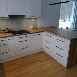 Jasna kuchnia z drewnianym blatem i czarnymi uchwytami, widok na okno z zimowym krajobrazem. Minimalistyczny design, nowoczesne oświetlenie.