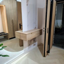 Nowoczesna szafa wnękowa z lustrem i oświetleniem LED, drewniane wykończenie, minimalistyczny design, drzwi wejściowe w tle, jasna podłoga w jodełkę.