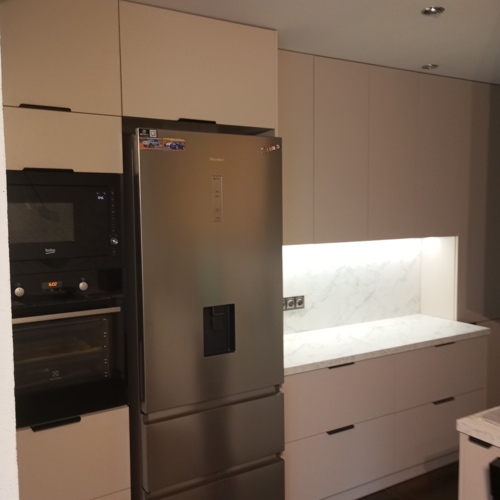 Jasna kuchnia z zabudową: lodówka Hisense, piekarnik Beko, biały blat z marmurowym wzorem i minimalistyczne uchwyty szafek. Nowoczesny design.