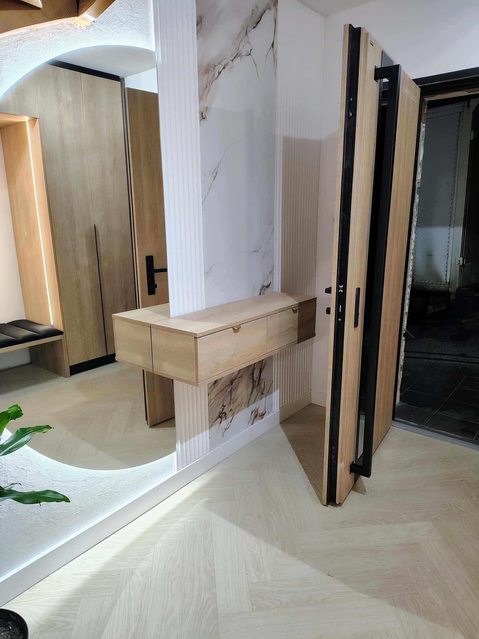 Nowoczesna szafa wnękowa z lustrem i oświetleniem LED, drewniane wykończenie, minimalistyczny design, drzwi wejściowe w tle, jasna podłoga w jodełkę.