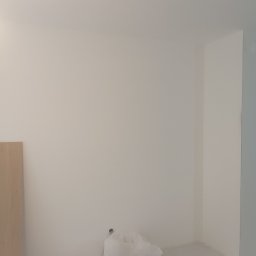 Jakub Jabłoński - Przygotowane do malowania wnętrze: białe ściany po szpachlowaniu, zabezpieczona folią podłoga, widoczne listwy przypodłogowe i fragment płyty.