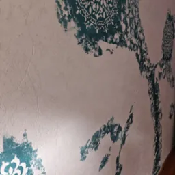 Dekoracyjna ściana z efektem przetarć, z motywami mandali w odcieniach turkusu na teksturowanym, jasnym tle. Artystyczne wykończenie wnętrza, widok z perspektywy.