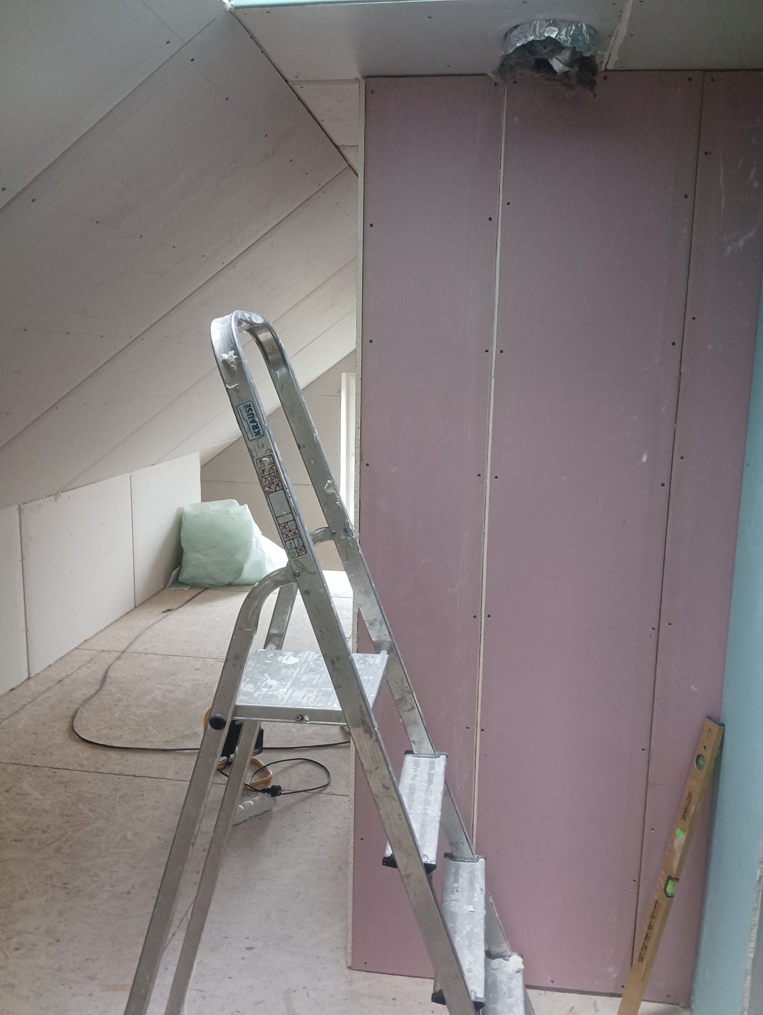 Montaż płyt kartonowo-gipsowych na poddaszu, widoczna aluminiowa drabina Krause i poziomica