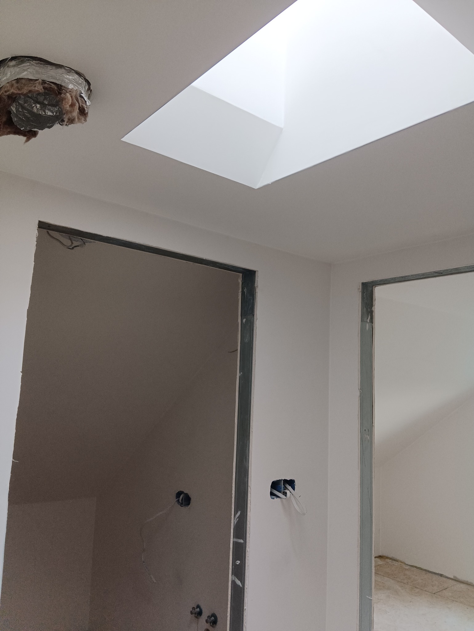 Wnętrze w trakcie prac w Białymstoku: widoczny fragment ocieplenia na suficie, otwór okienny w suficie, ściany przygotowane do dalszych prac, widoczne otwory na instalacje elektryczne.