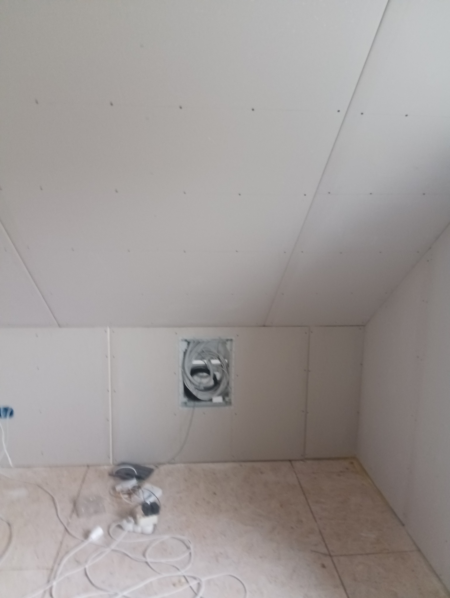 Poddasze z zamontowaną płytą karton-gips, widoczne łączenia płyt i otwór z kablami, przygotowane do dalszych prac wykończeniowych.