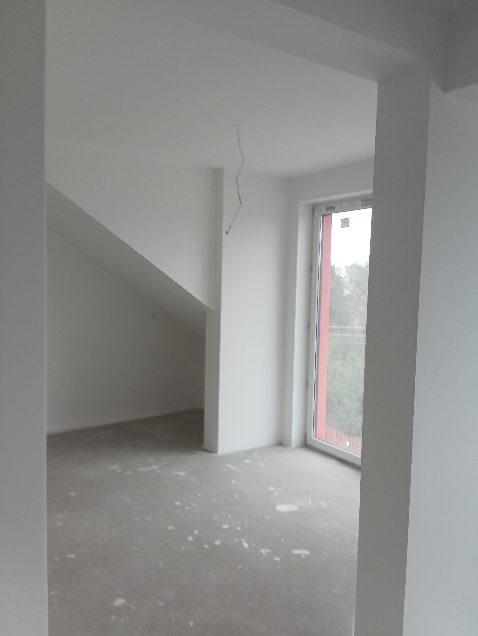 Wnętrze w trakcie malowania w Białymstoku, ściany i sufit świeżo pomalowane na biało, widoczne ślady farby na podłodze, okno z czerwoną ramą.