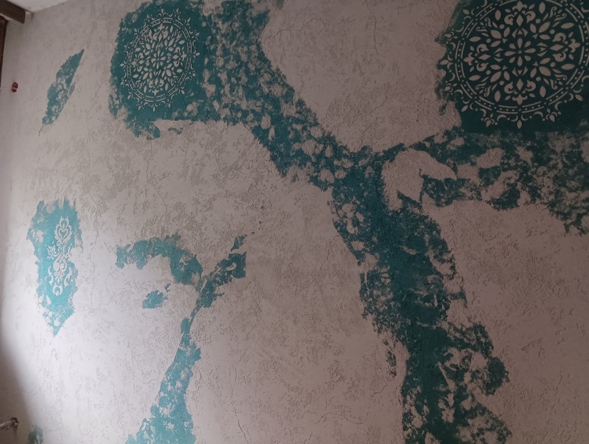 Dekoracyjna ściana z turkusowymi wzorami mandali i nieregularnymi plamami na teksturowanym, jasnym tle. Unikalna technika malarska.