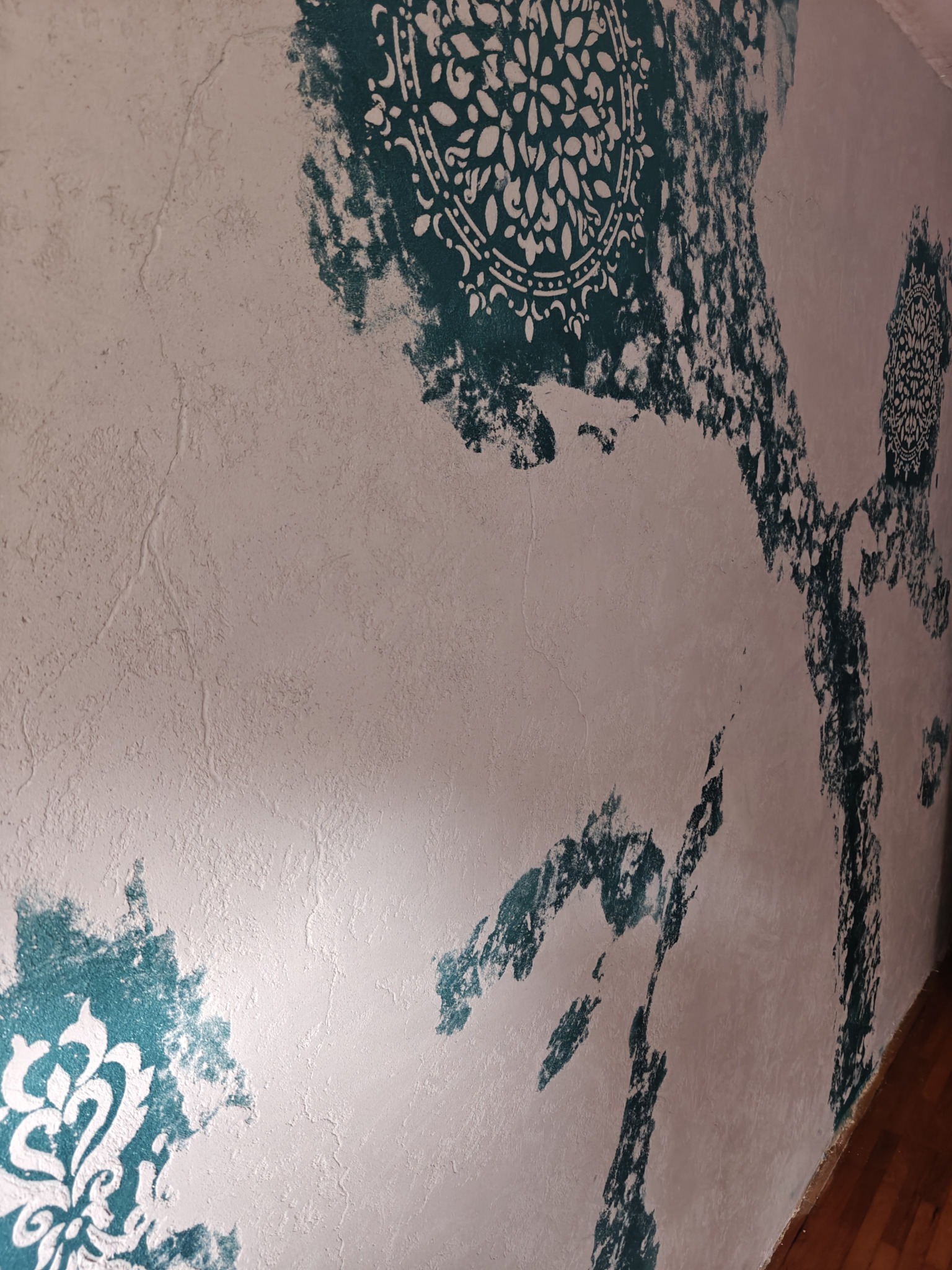 Dekoracyjna ściana z efektem przetarć, z motywami mandali w odcieniach turkusu na teksturowanym, jasnym tle. Artystyczne wykończenie wnętrza, widok z perspektywy.