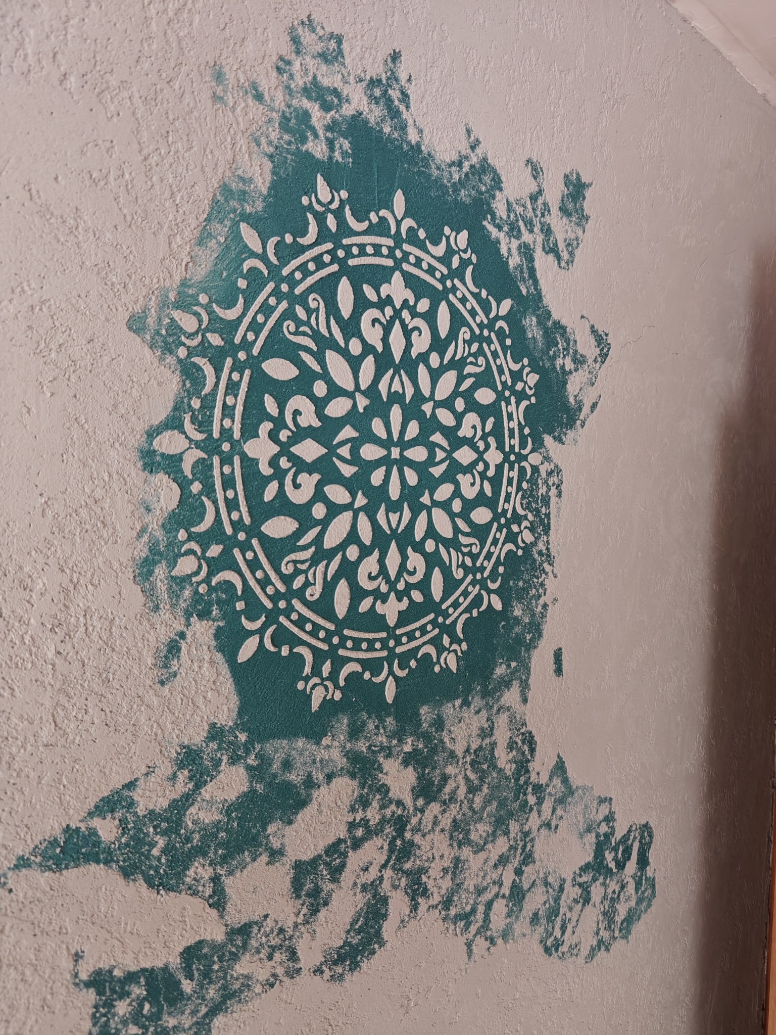 Teksturowana ściana z dekoracyjnym, turkusowym wzorem mandali. Biały ornament na nierównej powierzchni. Efektowna dekoracja wnętrza w zbliżeniu.