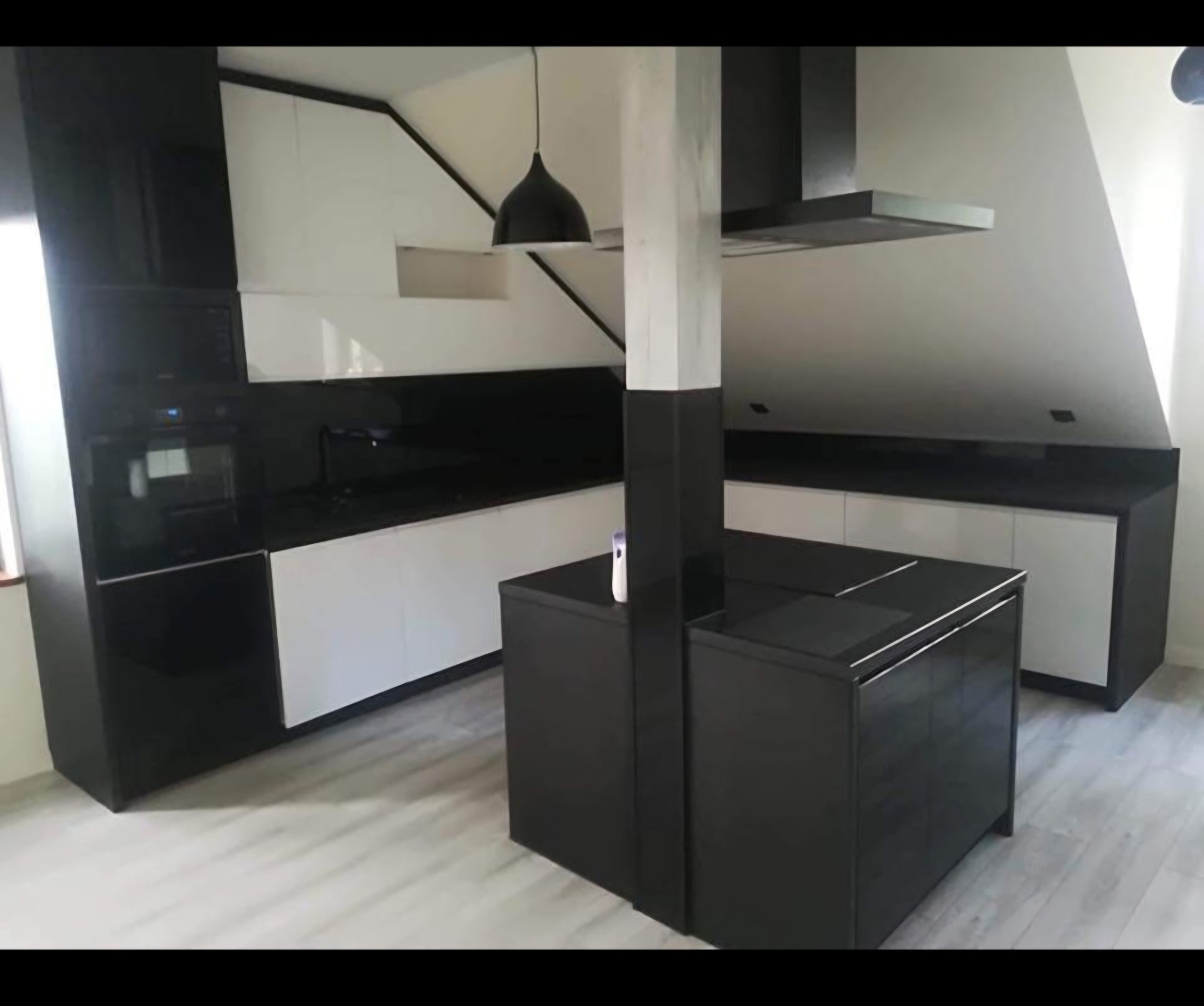 Nowoczesna kuchnia w czarno-białej kolorystyce z wyspą kuchenną, oświetleniem punktowym i skośnym sufitem.