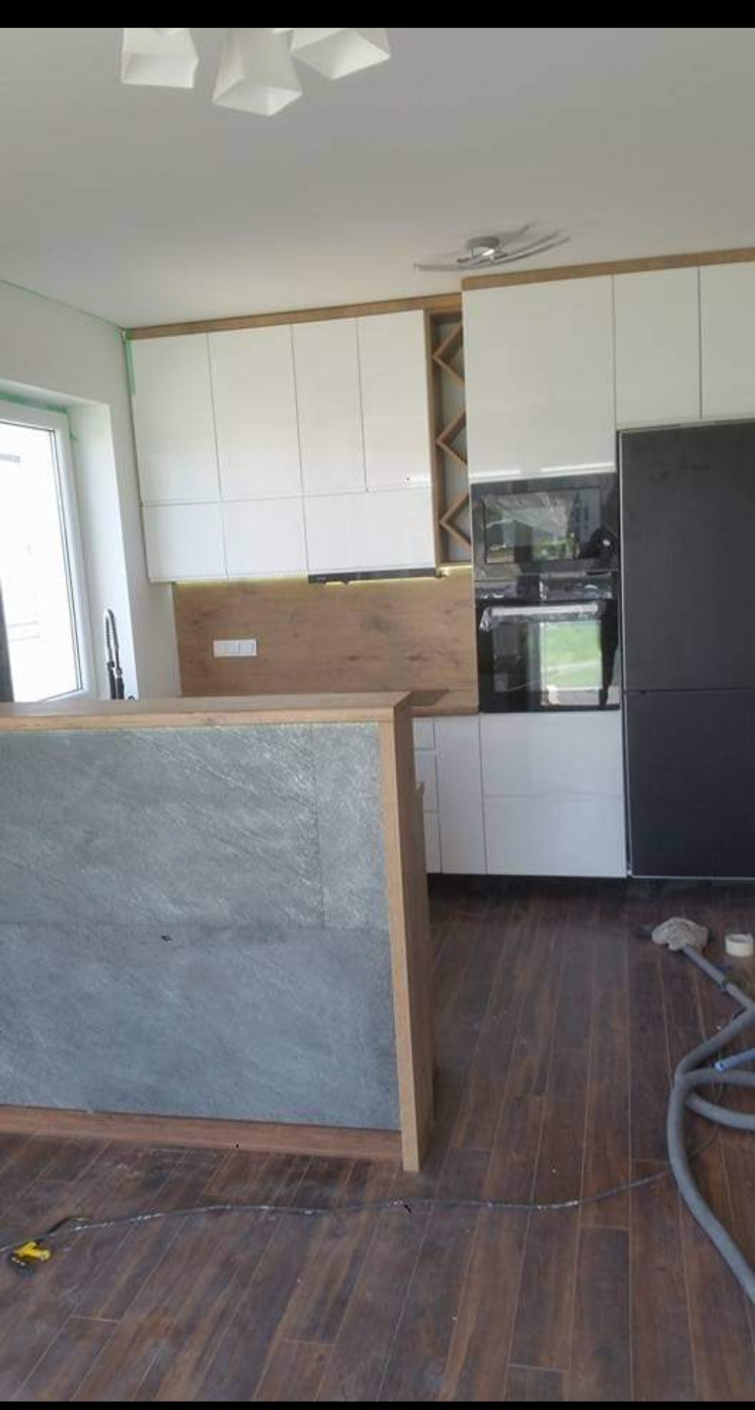 Montaż białych szafek kuchennych z drewnianymi akcentami w Białymstoku, widoczny fragment wyspy kuchennej z szarym blatem i niedokończone panele podłogowe.