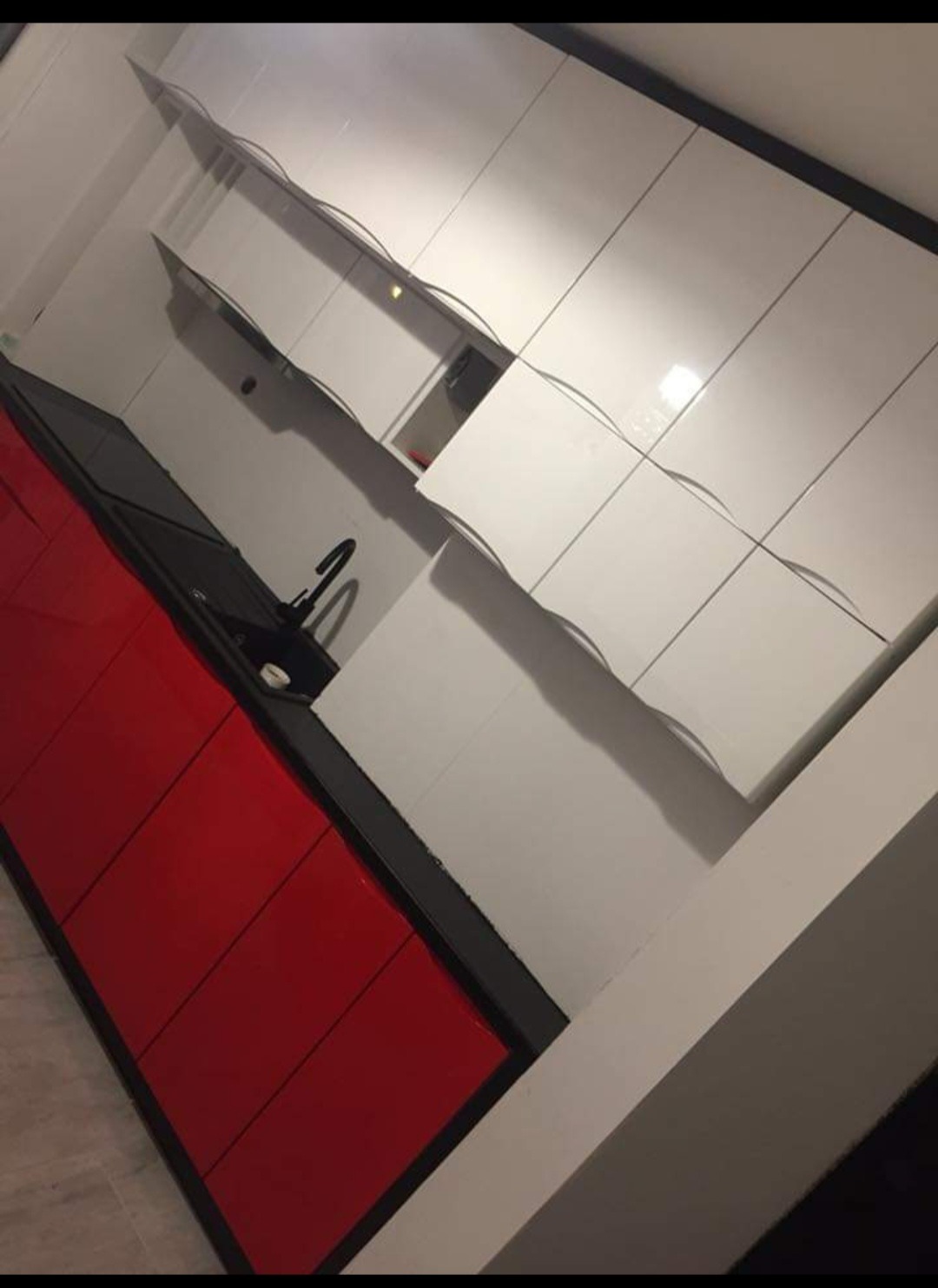 Nowoczesna kuchnia z białymi szafkami górnymi z subtelnymi uchwytami i czerwonymi szafkami dolnymi pod czarnym blatem, widok pod kątem.