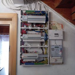 Mateusz Fryzowicz - Rozdzielnia elektryczna w domu jednorodzinnym, widok z bliska na zamontowane bezpieczniki, kable i licznik energii. Nowa instalacja, po zakończeniu prac.