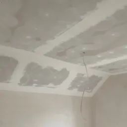 Sufit podwieszany z płyt gipsowo-kartonowych w trakcie szpachlowania, widoczny przewód elektryczny zwisający z otworu, niedokończone połączenia płyt.